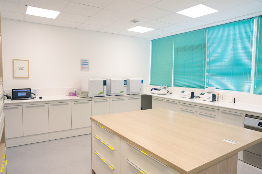 Salle de stérilisation du cabinet avec trois autoclaves et des appareils alignés sur un plan de travail, et un grand îlot en bois à tiroirs au premier plan